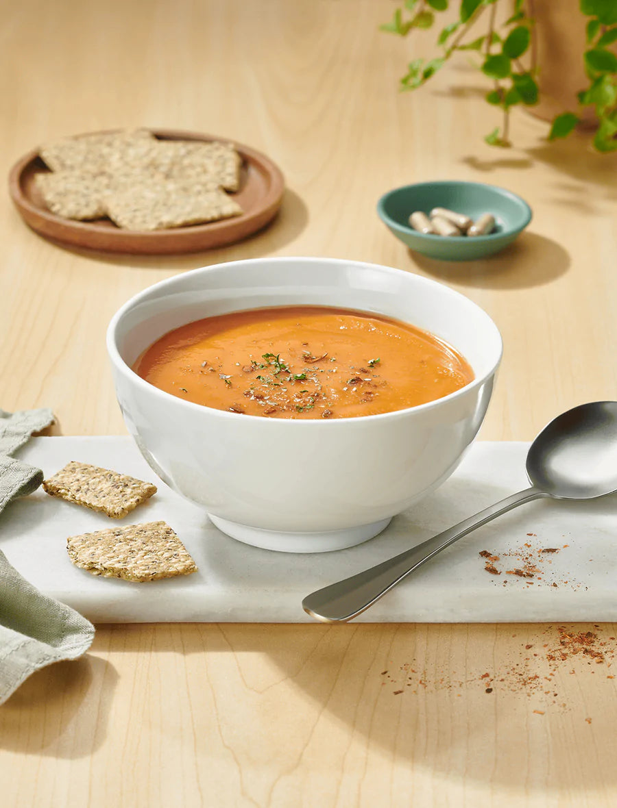 Bowl of orange ProLon soup with kale crackers on a wooden table