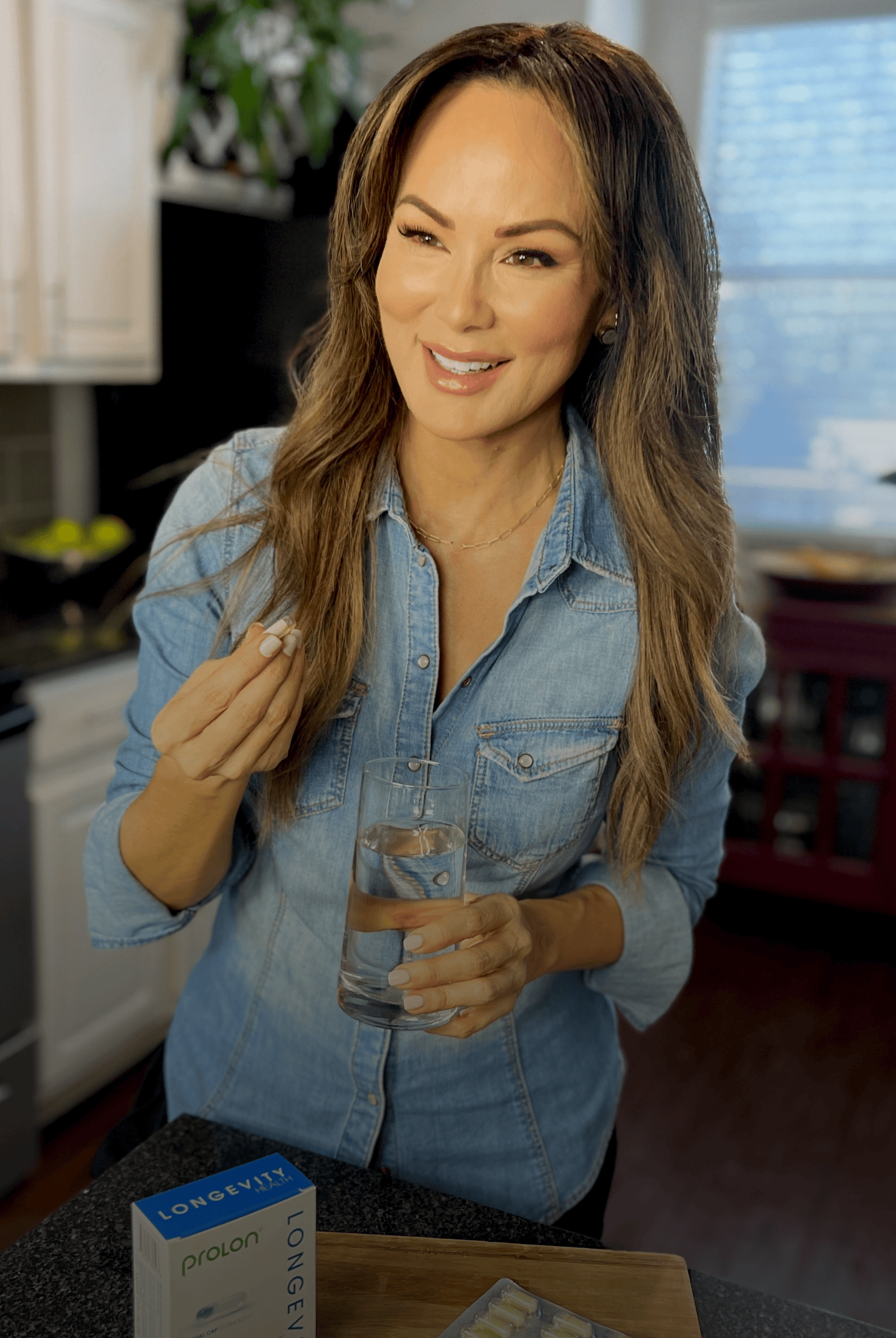 Smiling woman in a denim shirt holding a glass in her kitchen next to a ProLon box